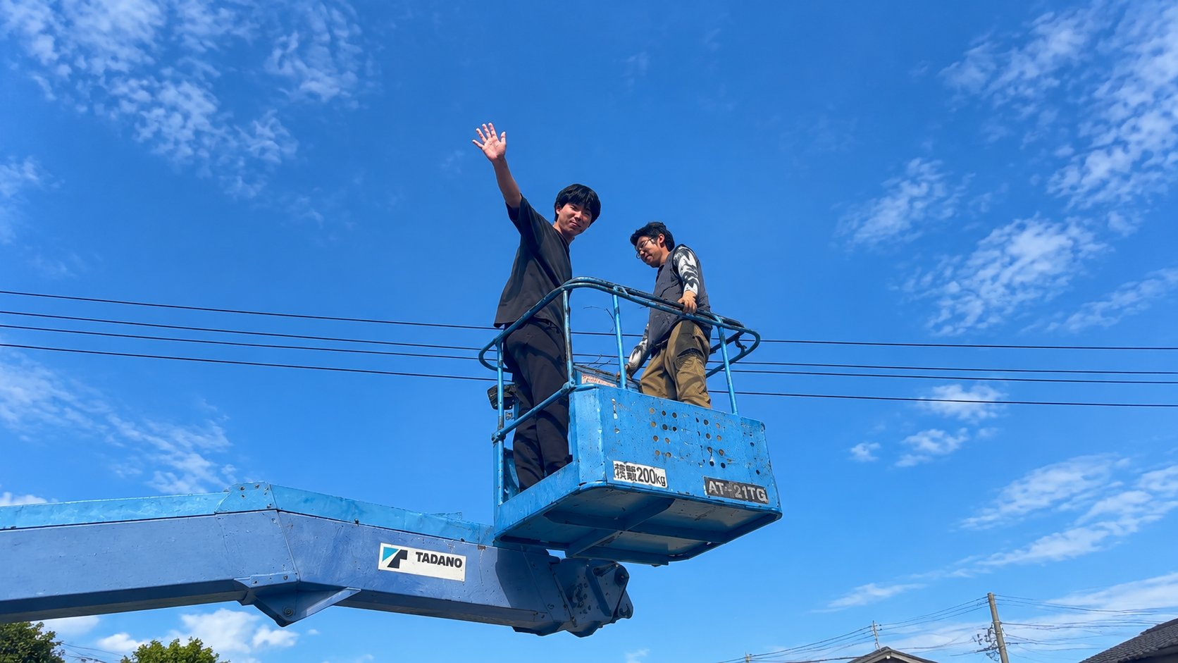高所作業車の上から手を振る社員
