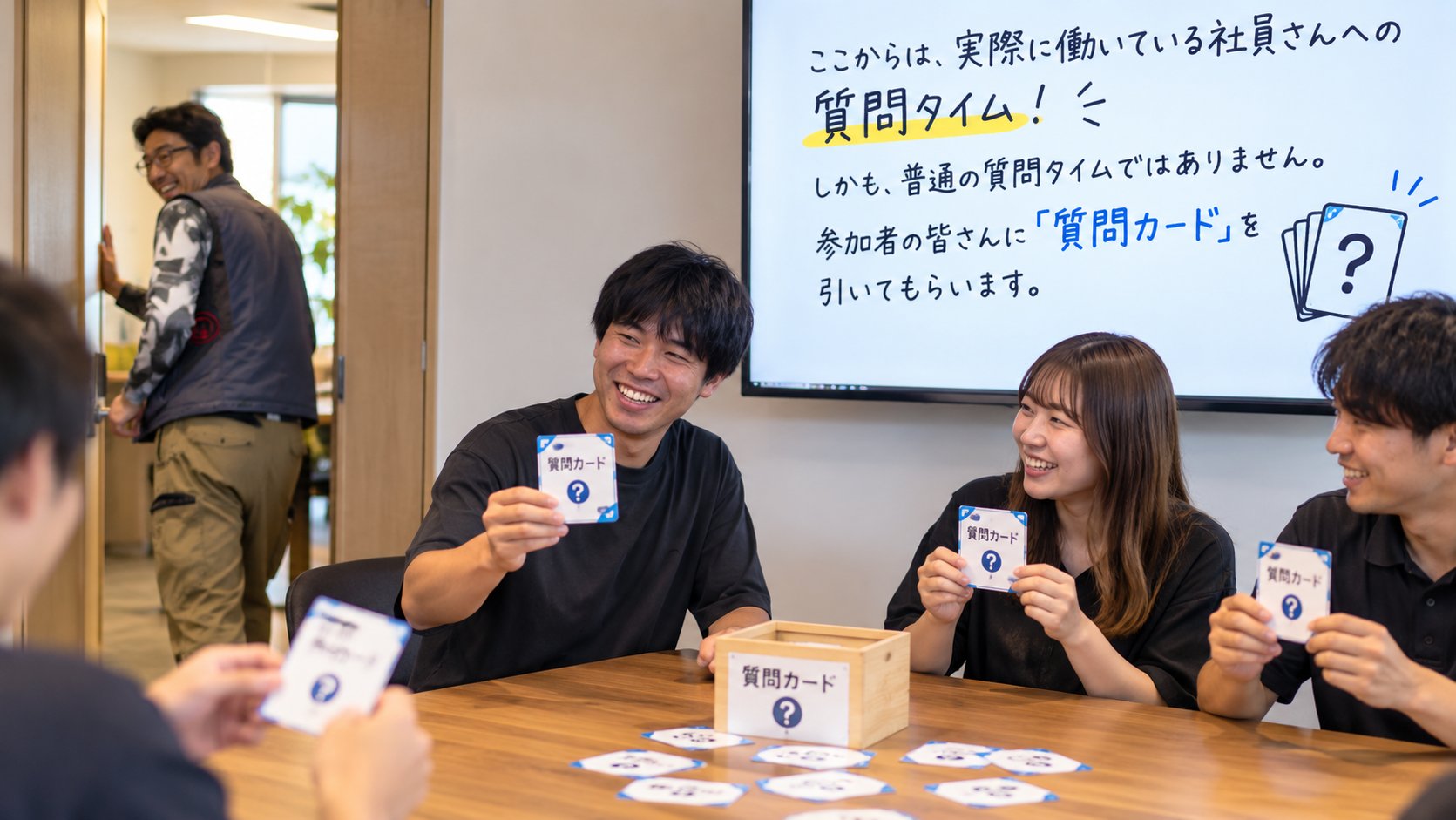 質問カードを手に談笑する社員と、部屋の外からのぞく社長